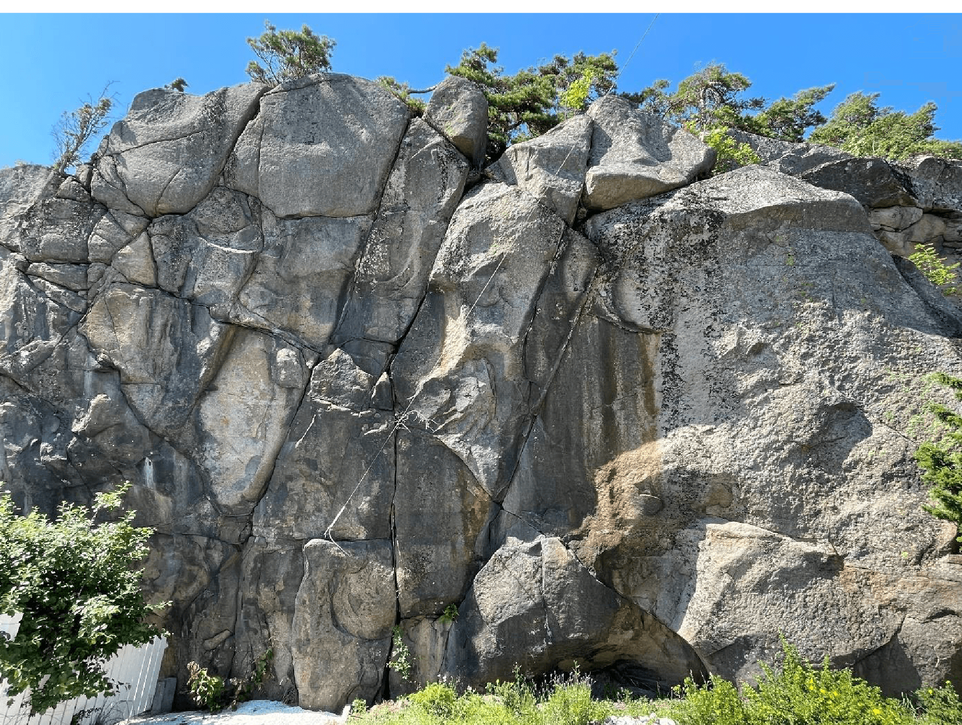 Høy, oppsprukket bergskrent med store steinblokker og vegetasjon på toppen, langs Kyststien ved Faratangen.