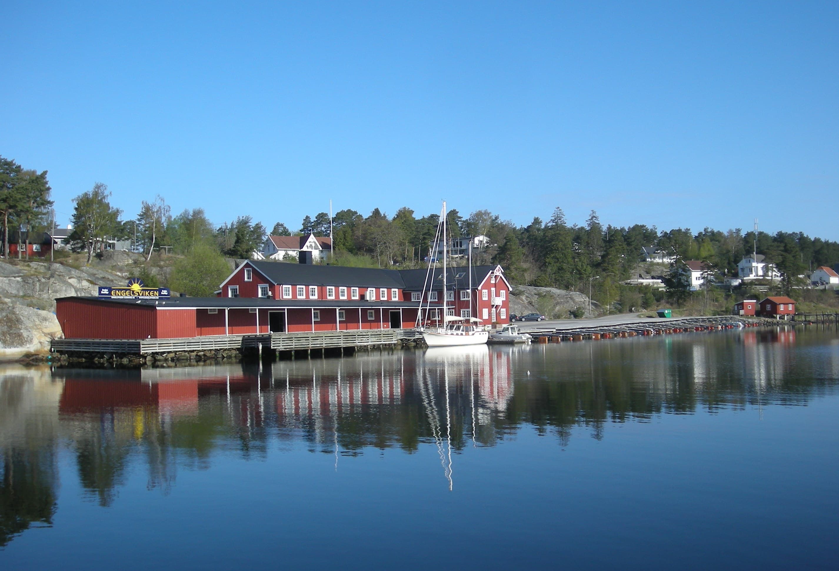 Stille kysthavn i Onsøy med røde sjøboder, en fortøyd seilbåt og molo.